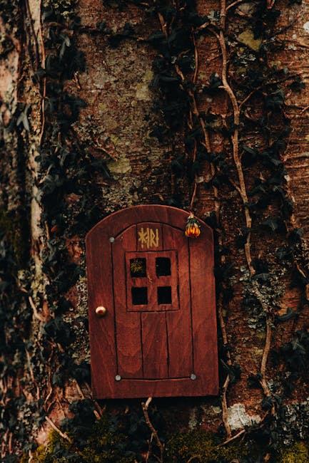 A handcrafted wooden fairy door mounted on a moss-covered tree trunk with ivy growing around it