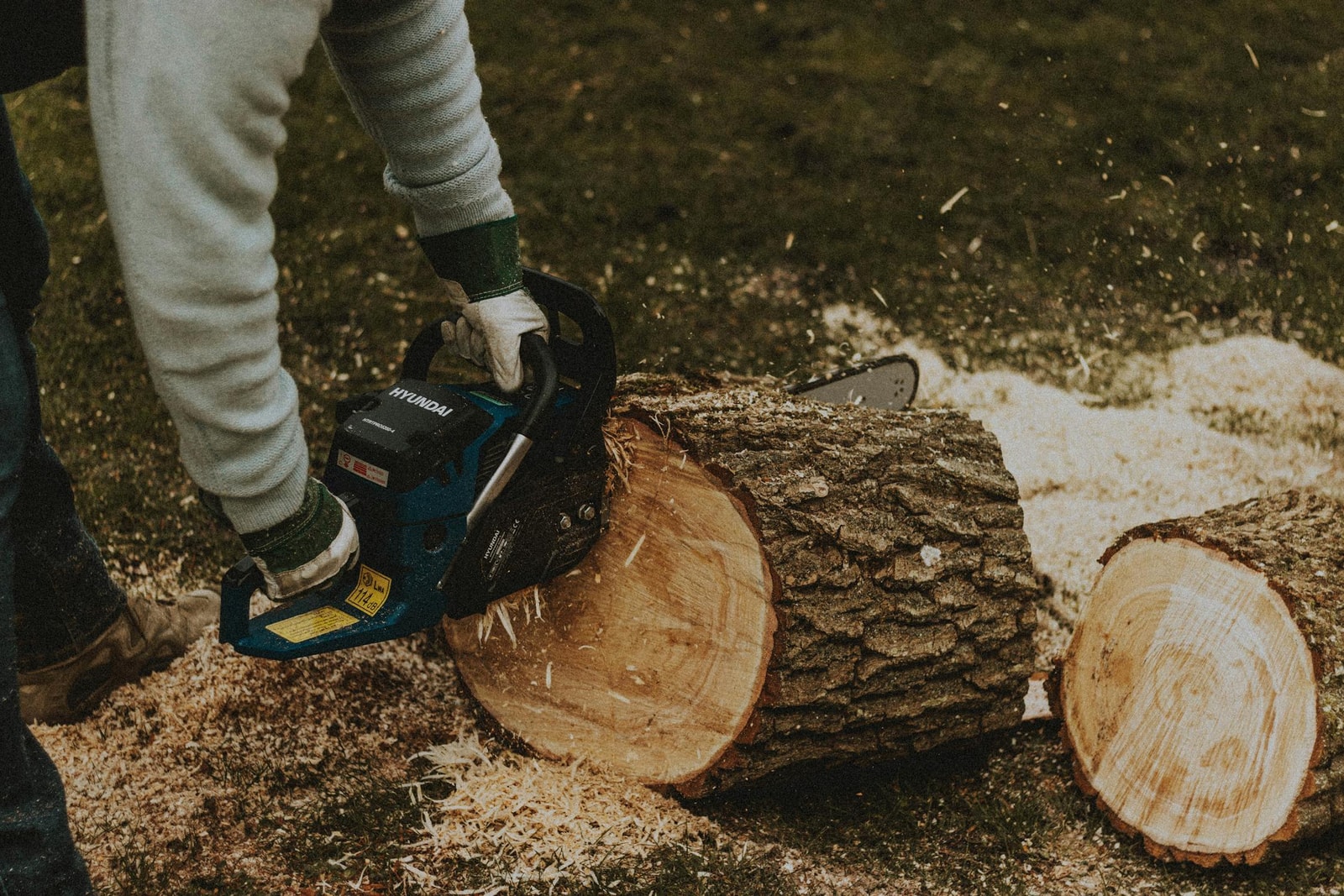 Man using a chainsaw to cut through a log in a suburban yard