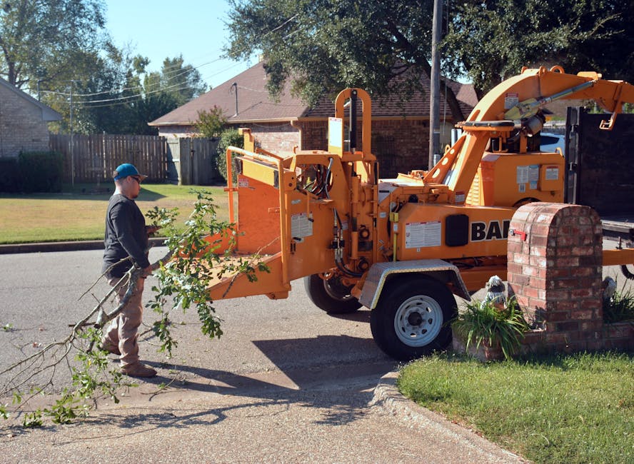 Tree service worker feeding branches into a wood chipper on a residential street